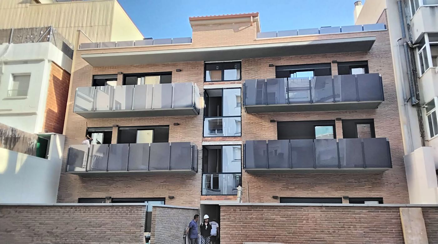 Fachada principal de ladrillo con terrazas de vidrio oscuro y núcleo de escalera acristalado