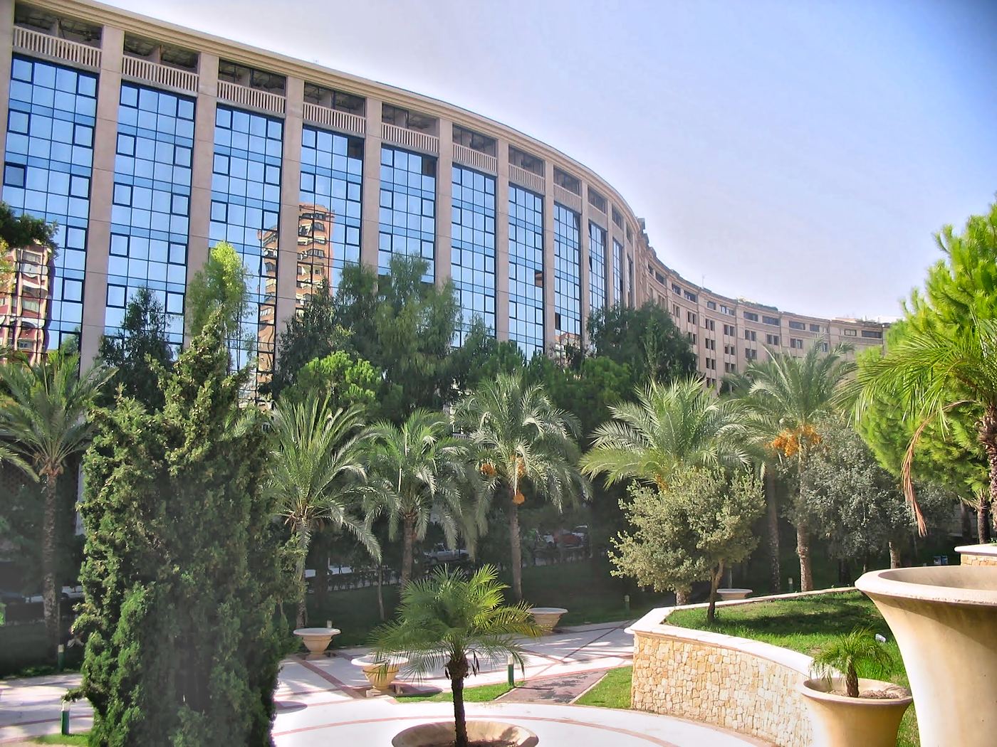 El edificio de fachada curva visto desde los jardines con palmeras