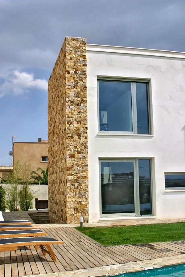 Volumen blanco junto a un muro de piedra, con tarima y césped