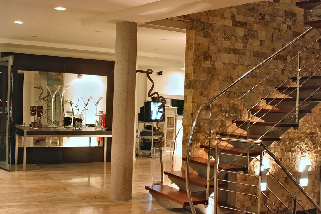 Salón con escalera de madera y acero junto a un muro de piedra