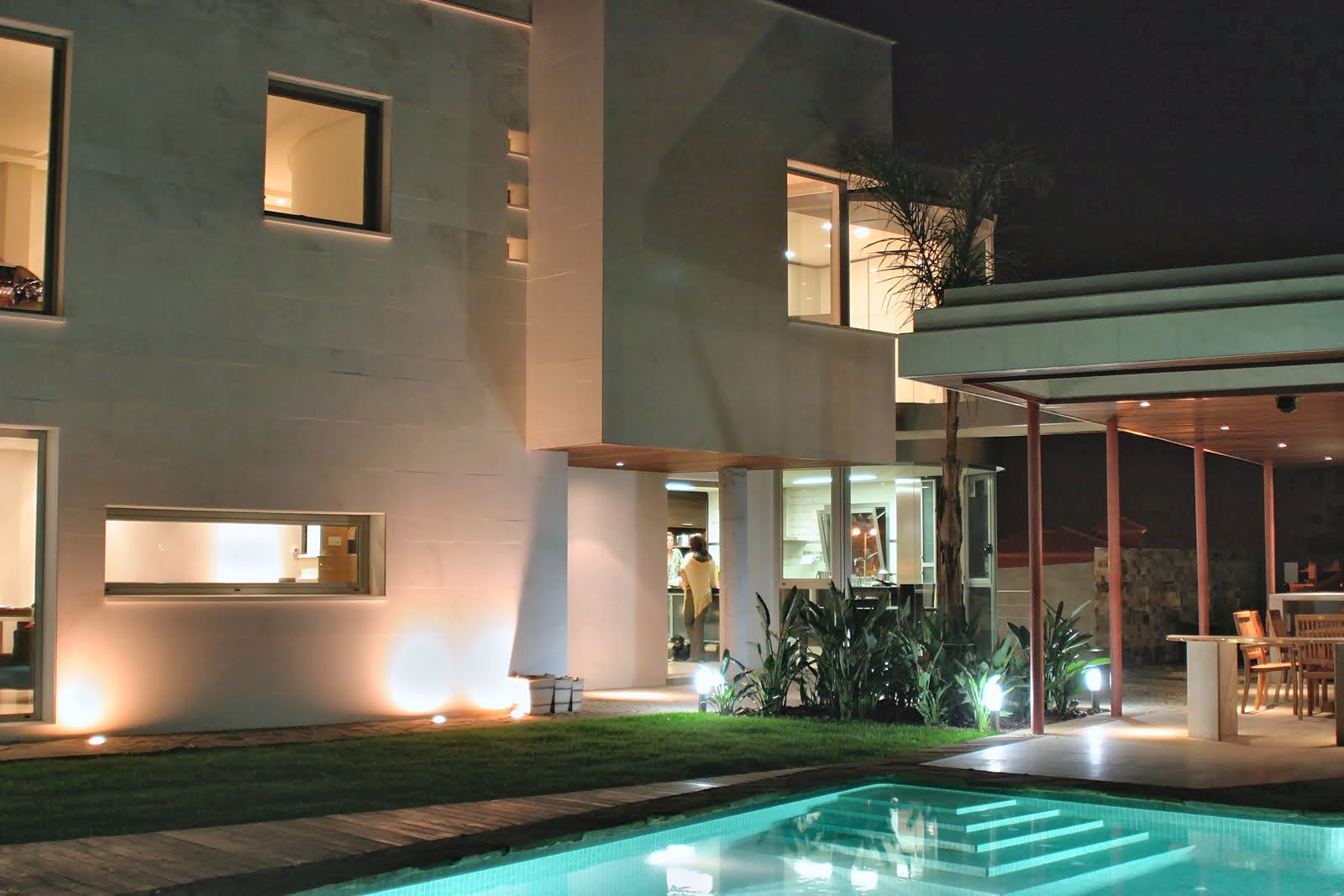 Vivienda unifamiliar iluminada de noche, con la piscina